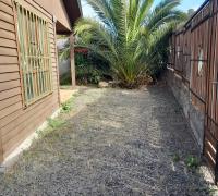 “Vista del antejardín lateral de la propiedad, donde se aprecia el portón de acceso principal construido en madera y metal.