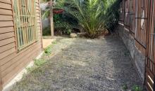 “Vista del antejardín lateral de la propiedad, donde se aprecia el portón de acceso principal construido en madera y metal.