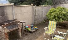 “Sector de asadera dentro del patio, acompañado de un área despejada ideal para reuniones al aire libre y delimitado por cierre perimetral de hormigón.”