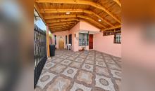 Acceso techado de la casa, con piso de baldosas y estructura de madera.
