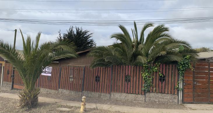 “Frontis de un terreno con dos casas, cercado con un portón corredero de madera y metal.