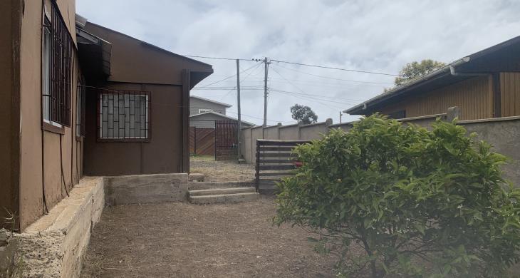  “Vista del patio lateral despejado, donde se observa la primera vivienda de un piso y la segunda vivienda de dos niveles al fondo.
