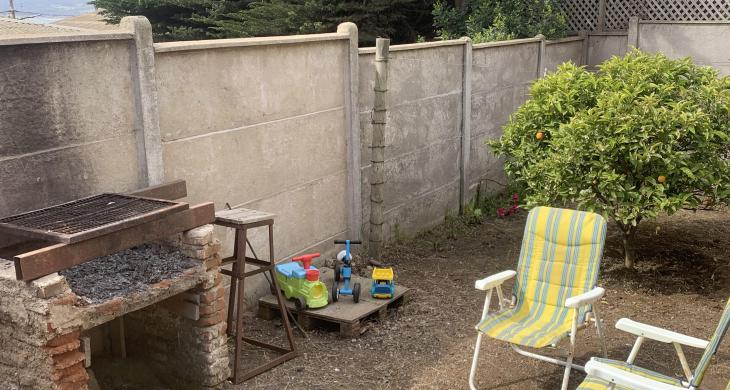 “Sector de asadera dentro del patio, acompañado de un área despejada ideal para reuniones al aire libre y delimitado por cierre perimetral de hormigón.”